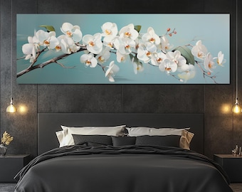 Puede incluir: Una impresión en lienzo rectangular que presenta una rama de orquídeas blancas sobre un fondo azul claro. Las orquídeas tienen centros amarillos y están dispuestas sobre una rama marrón. La obra de arte se exhibe sobre una cama con ropa de cama negra.