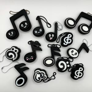May include: A collection of black and white musical note and treble clef keychains with various facial expressions. Each keychain has a silver chain. The musical notes and treble clefs are in different shapes and sizes.
