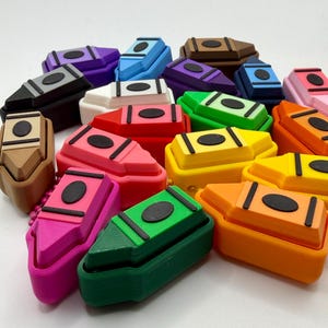 May include: A collection of colorful crayon-shaped objects in various colors, including pink, green, yellow, and orange. Each crayon has a black oval and rectangular accents on top. The crayons are scattered, creating a playful and vibrant display.