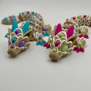 May include: Two small, hand-painted ceramic dragons with white, brown, green, pink, purple, and blue details. The dragons are in a curled up position.