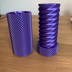 May include: Two purple 3D printed cylindrical objects. One object has a smooth, spiral design. The other object has a textured, diamond-shaped pattern.