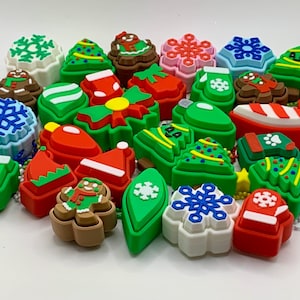 May include: A selection of colourful Christmas-themed charms in various shapes, including Christmas trees, snowflakes, and gingerbread men. The charms are red, green, white, and brown, with silver chain attachments.