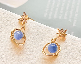 May include: A pair of gold earrings with a blue gemstone in the center of a gold ring. Each earring has a star-shaped charm with clear rhinestones.