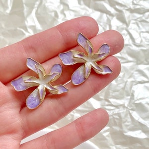 May include: A pair of gold-tone earrings with a purple and white flower design.