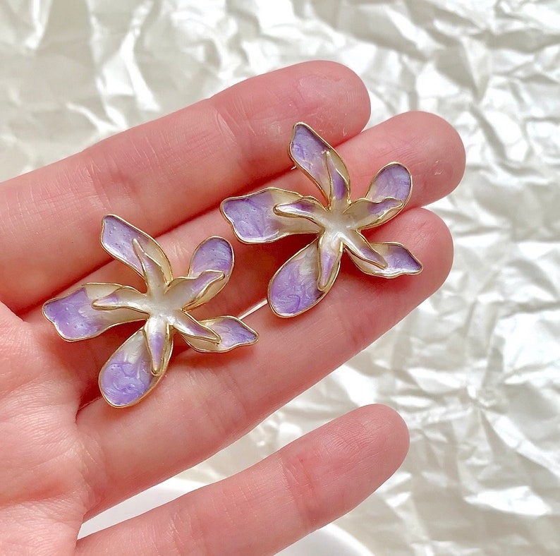 May include: A pair of gold-tone earrings with a purple and white flower design.