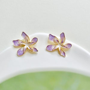 May include: A pair of purple and gold flower-shaped earrings. The earrings are made of metal and have a delicate, feminine design.