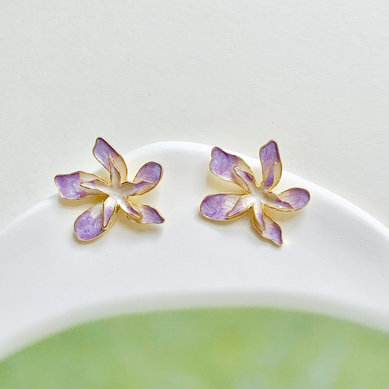 May include: A pair of purple and gold flower-shaped earrings. The earrings are made of metal and have a delicate, feminine design.