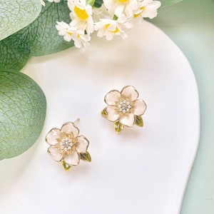 May include: A pair of gold-tone flower earrings with white enamel and clear rhinestone accents.