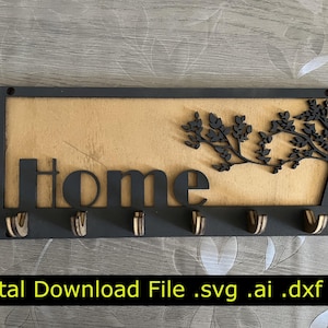 May include: A wooden key holder with the word "home" cut out in black, featuring a tree design and six key hooks. The background is a light wood color, and the frame is black. The text "Digital Download File .svg .ai .dxf .pdf" is at the bottom.