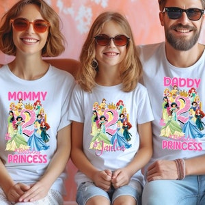 May include: A family of three wearing white t-shirts with a Disney Princess theme. The shirts feature a group of princesses, including Cinderella, Ariel, Belle, and Snow White. The shirts also have the text "Mommy", "Daddy", and "Birthday Princess" on them. The shirts are a fun way to celebrate a birthday.
