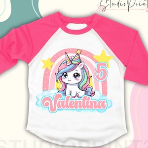 Peut inclure: Un t-shirt à manches longues blanc et rose avec un motif arc-en-ciel et licorne. La licorne porte un chapeau de fête et le texte "Valentina" est écrit sur le t-shirt. Le chiffre "5" est également sur le t-shirt.
