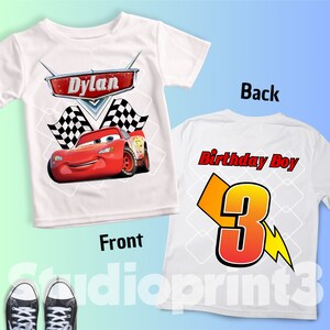 May include: White t-shirt featuring a red race car graphic with the name "Dylan" above it. The front of the shirt also has checkered flags. The back of the shirt says "Birthday Boy" with a number 3 and a lightning bolt.