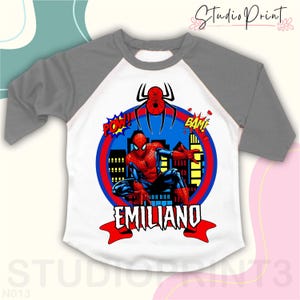 May include: A white and gray baseball t-shirt with a red and blue Spiderman graphic. The graphic includes the words "POW!" and "BAM!" and the name "EMILIANO".