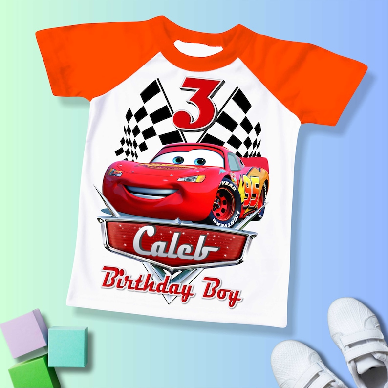 May include: White t-shirt with a red race car, checkered flags, and the number 3. The text "Caleb Birthday Boy" is printed on the shirt.