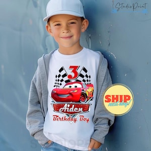 Puede incluir: Camiseta blanca con un coche de carreras rojo, banderas a cuadros y el n&uacute;mero 3. El texto "Aiden Birthday Boy" est&aacute; impreso debajo del coche.