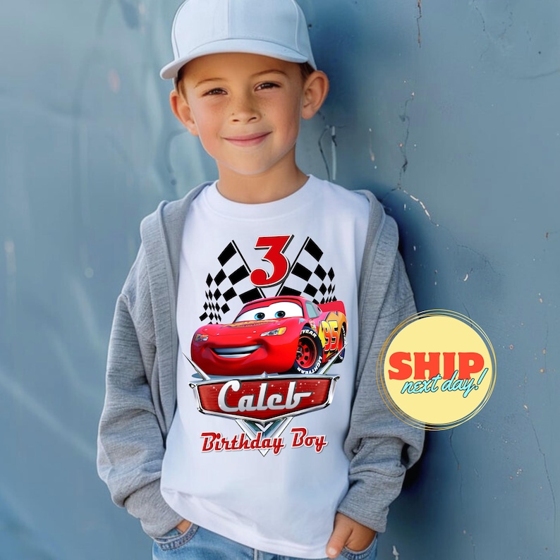 May include: White t-shirt with a red race car, checkered flags, and the number 3. The text "Caleb Birthday Boy" is printed below the car.