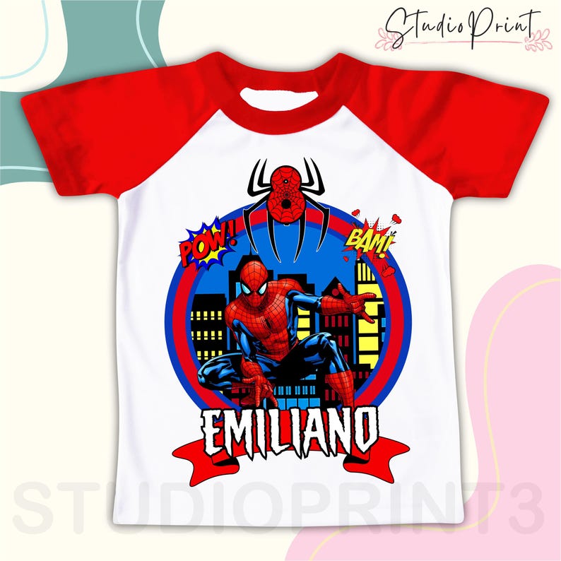 May include: White and red raglan t-shirt with a Spiderman graphic. The graphic features Spiderman in a city scene with the words "POW!" and "BAM!" and the name "EMILIANO" below.