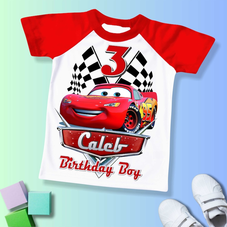 May include: Red and white t-shirt with a red race car, checkered flags, and the number 3. The text "Caleb Birthday Boy" is printed on the shirt.