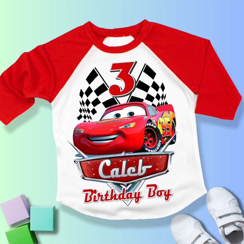 May include: Red and white baseball style t-shirt with a red race car, checkered flags, and the number 3. The text "Caleb Birthday Boy" is printed on the shirt.