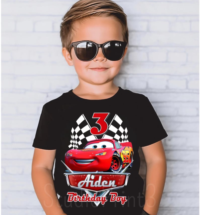 Puede incluir: Camiseta negra con un gr&aacute;fico de coche de carreras rojo, banderas a cuadros y el n&uacute;mero 3. El texto "Aiden Birthday Boy" est&aacute; debajo del coche.
