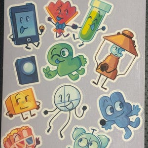 May include: A sticker sheet featuring cartoon characters, including a blue phone, a red fan, a green test tube, and a yellow lamp. The text "object show hosts" is at the top. The artist's signature, "emmkitt doodles", is at the bottom.