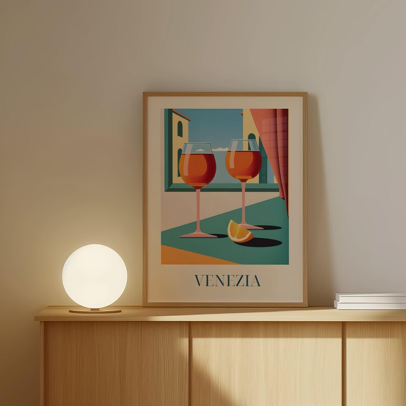 a framed poster of two wine glasses with orange slices, placed on a wooden shelf next to a round table lamp.