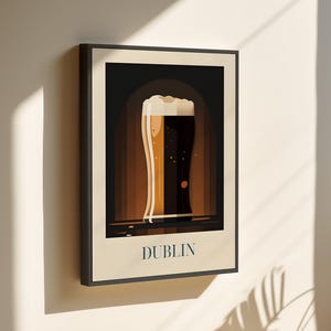 May include: A framed illustration of a glass of beer with a white head, set against a dark brown background. The text "DUBLIN" is printed in white at the bottom of the image.