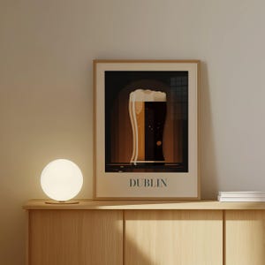 a framed poster of a glass of beer with the word "DUBLIN" written on it, placed on a wooden shelf or cabinet.
