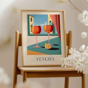 a framed illustration of two wine glasses with orange slices, set against a backdrop of a building and a window, with the word "VENEZIA" written below the illustration.