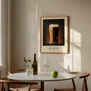 a dining table with a white tablecloth, a green bottle, a wine glass, and a green apple. Above the table, there is a framed poster of a beer glass with the word "Dublin" written on it.