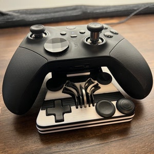 May include: A black Xbox controller with a white and black striped stand. The controller has a black and white patterned faceplate and a black and white striped grip.