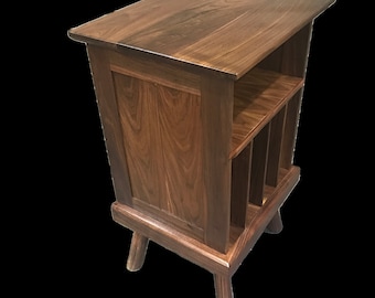 Peut inclure: Un meuble en bois brun foncé pour ranger des disques vinyles, avec trois pieds et une étagère. Le meuble a une finition lisse et polie et un design simple et élégant.