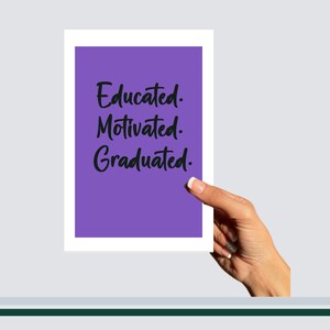 May include: A white-framed card with a purple background, featuring the words "Educated. Motivated. Graduated." in black script. The card is held by a hand against a light gray background, suggesting a graduation theme.
