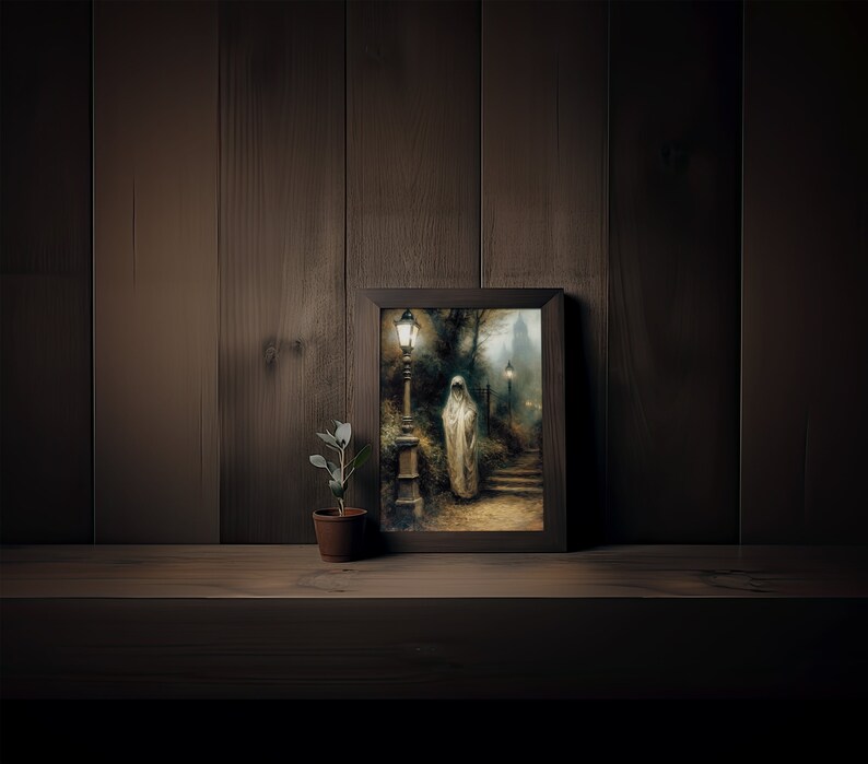 Op de afbeelding: Een ingelijst schilderij van een vrouw in een witte gewaden met capuchon die over een pad loopt dat verlicht wordt door lantaarns. Het schilderij is geplaatst tegen een donkere houten achtergrond.