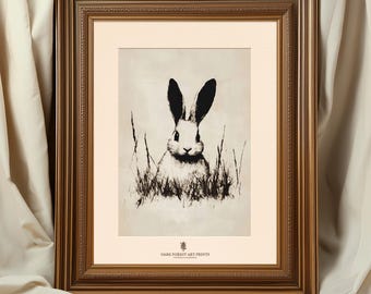 May include: Black and white illustration of a rabbit sitting in tall grass. The rabbit is looking directly at the viewer. The illustration is framed in a gold frame.