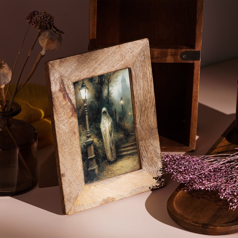 Op de afbeelding: Een houten fotolijst met een donkere, vintage-achtige print van een figuur in een witte jurk die in een mistige straat met lantaarns staat. De lijst heeft een lichtbruine houtkleur.