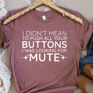 May include: A mauve t-shirt with the text "I didn't mean to push all your buttons I was looking for +MUTE+" in white.