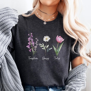 May include: A dark heather grey t-shirt with a floral design featuring a foxglove, daisy, and tulip. The flowers are labeled with their names.