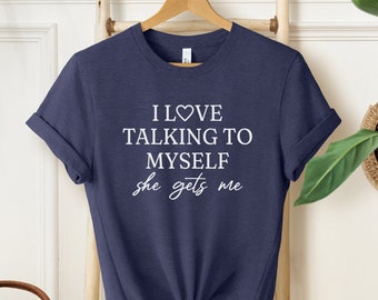 May include: A heather navy blue t-shirt with the text "I love talking to myself she gets me" in white lettering. The text includes a heart symbol.