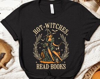 May include: Black t-shirt with a vintage-style graphic featuring a witch in a hat, sitting on a pumpkin, with the text "HOT WITCHES READ BOOKS". The design includes stars, bats, and a decorative border.
