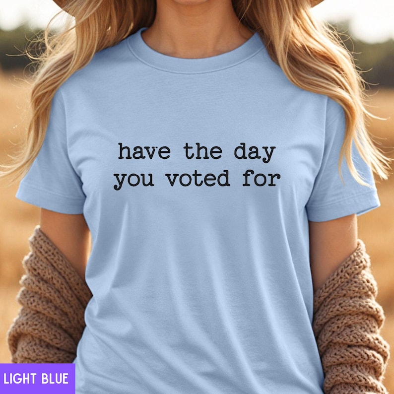 May include: Light blue t-shirt with the text "have the day you voted for" printed in black.