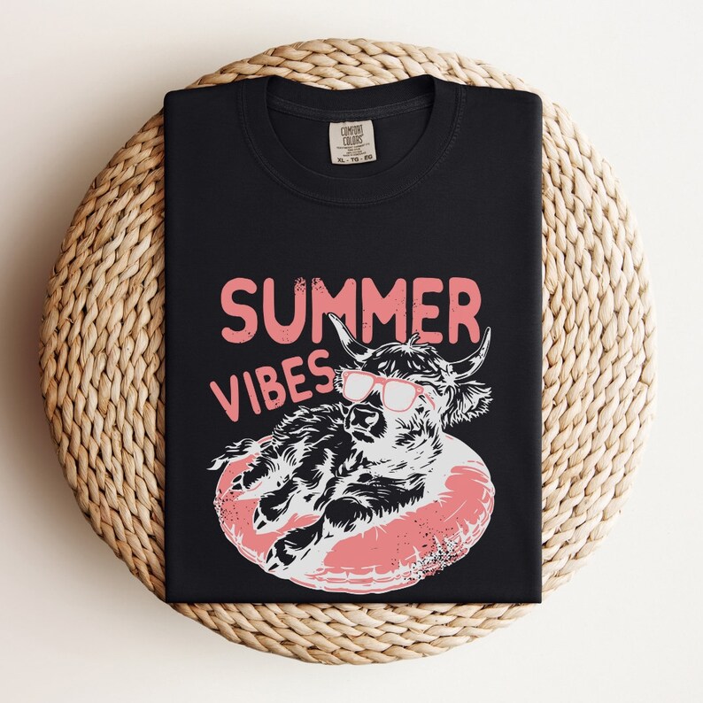 May include: Black t-shirt with a pink "Summer Vibes" graphic featuring a cartoon Highland cow wearing sunglasses and floating on a pink inflatable ring.
