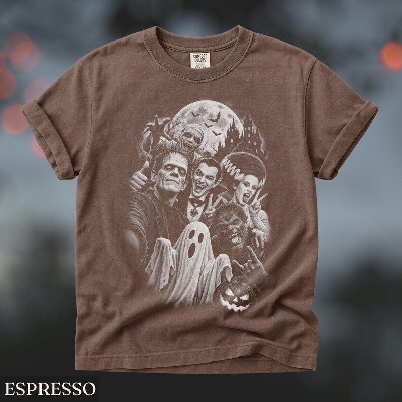 May include: A brown short-sleeve t-shirt featuring a white graphic print of classic horror movie monsters including Frankenstein, Dracula, a mummy, a werewolf, and a ghost, with a haunted castle and full moon in the background.