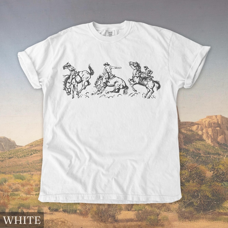 Puede incluir: Camiseta blanca con un dise&ntilde;o en blanco y negro de un vaquero montando un caballo salvaje. El dise&ntilde;o muestra una secuencia de tres im&aacute;genes del vaquero intentando mantenerse sobre el caballo. La palabra "WHITE" est&aacute; impresa en la parte inferior.