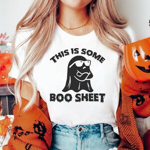 May include: White t-shirt with a black ghost wearing sunglasses and the text "This is some boo sheet".