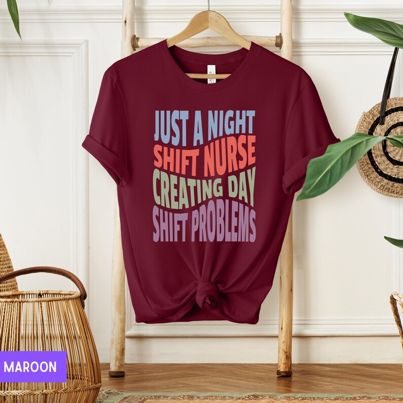 May include: A maroon t-shirt with the text "Just a night shift nurse creating day shift problems" in colourful letters.