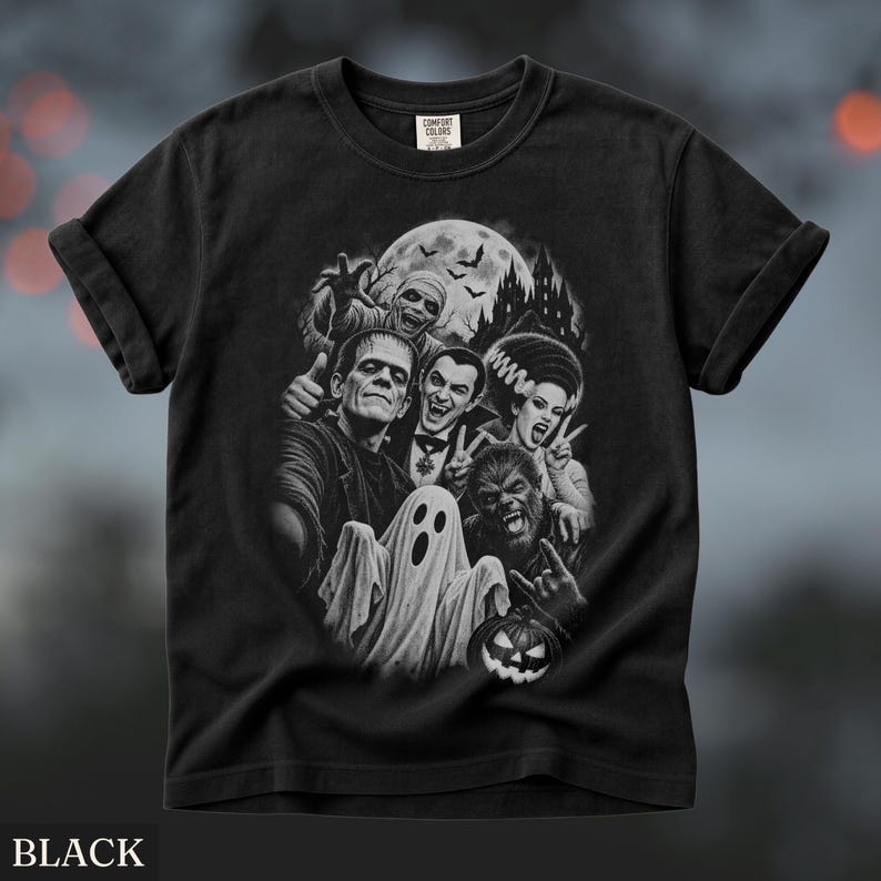 May include: A black short-sleeve t-shirt featuring a monochromatic graphic print of classic horror movie monsters including Frankenstein, Dracula, a mummy, a werewolf, and a ghost, set against a moonlit castle background with bats.