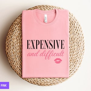 May include: Pink t-shirt with the text "EXPENSIVE and difficult" in black lettering and a pink lipstick print.