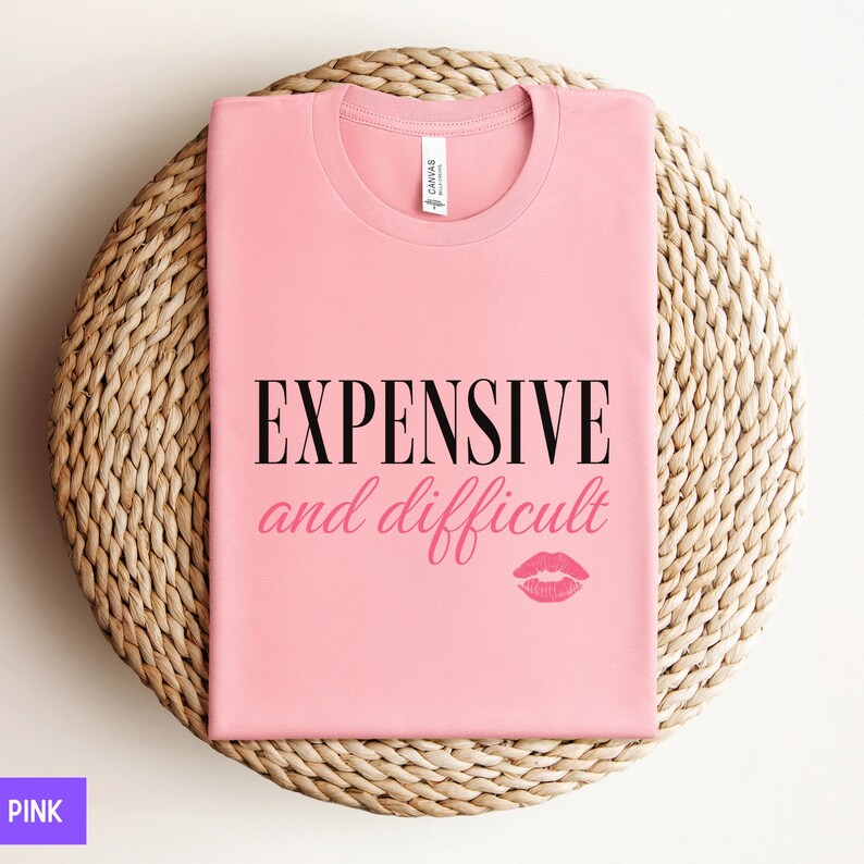 May include: Pink t-shirt with the text "EXPENSIVE and difficult" in black lettering and a pink lipstick print.