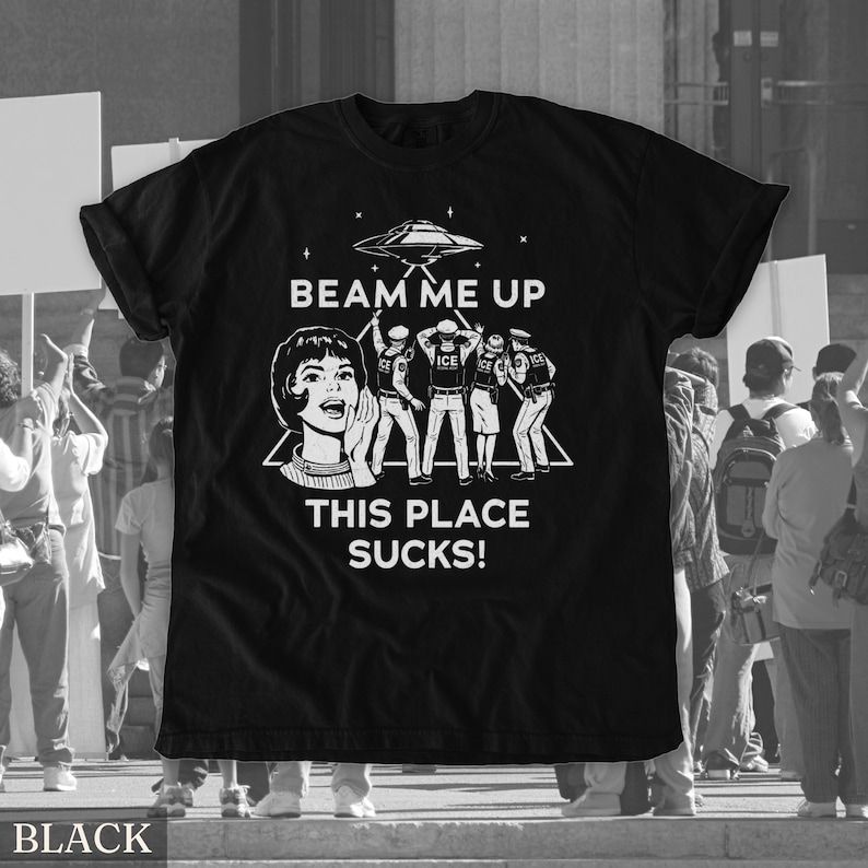 May include: Black t-shirt with a white graphic design. The design features a retro illustration of a woman, a UFO, and figures with the text "BEAM ME UP THIS PLACE SUCKS!"